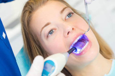 A dentist using an ultraviolet light to harden a filling