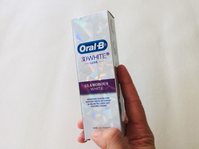 Holding the Oral-B 3D White Luxe Glamorous White Toothpaste in its box