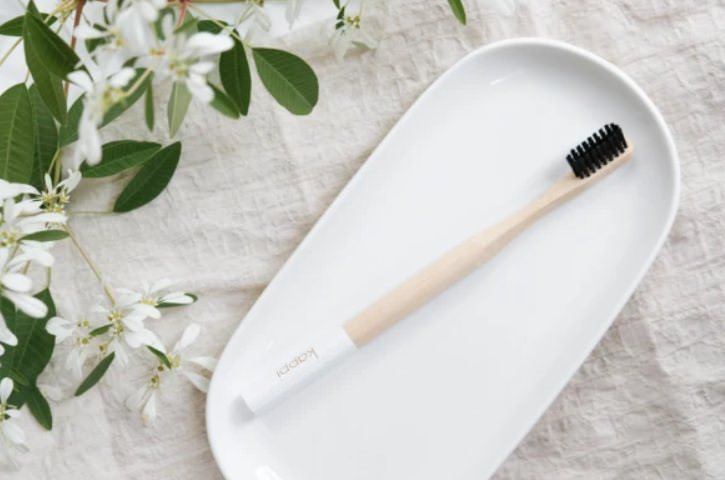 Kappi's bamboo toothbrush on a plate with flowers to the side