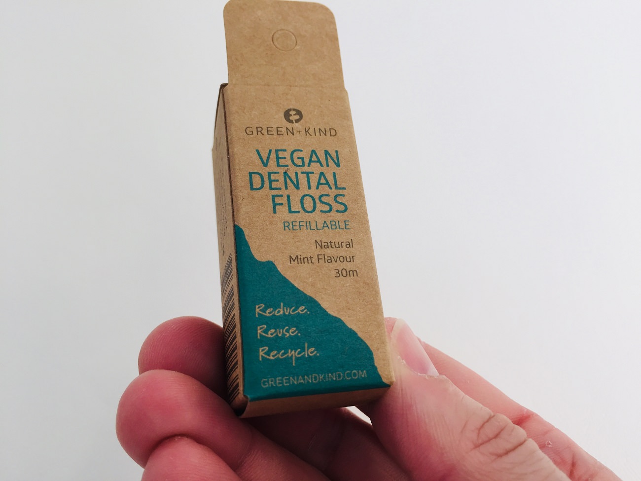 Holding the Green+Kind vegan dental floss packaging in my fingers