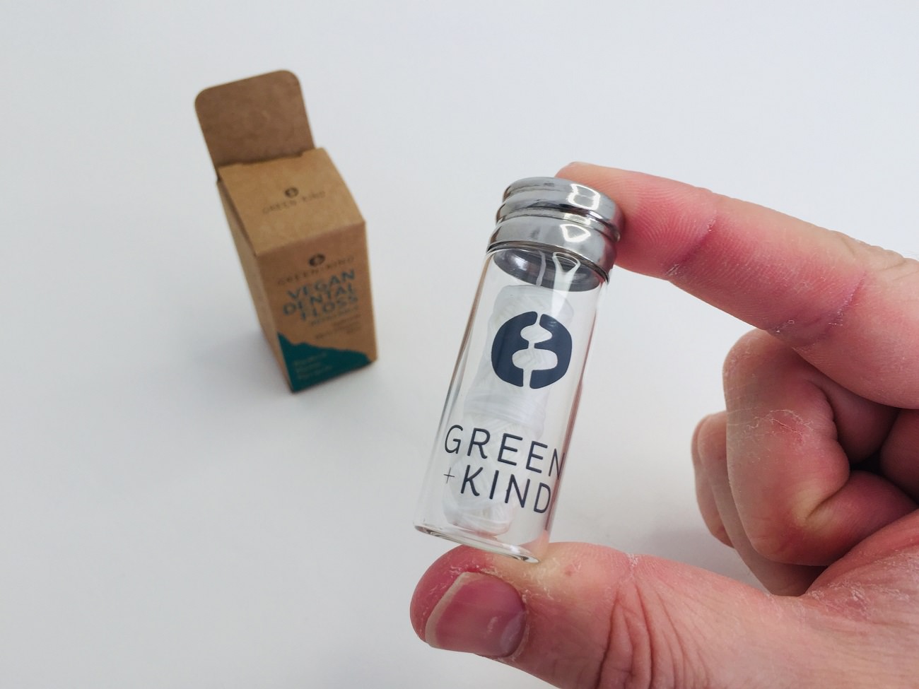 Holding the glass vial of Vegan floss by Green + Kind