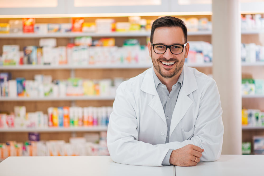 A male pharmacist with medication behind him